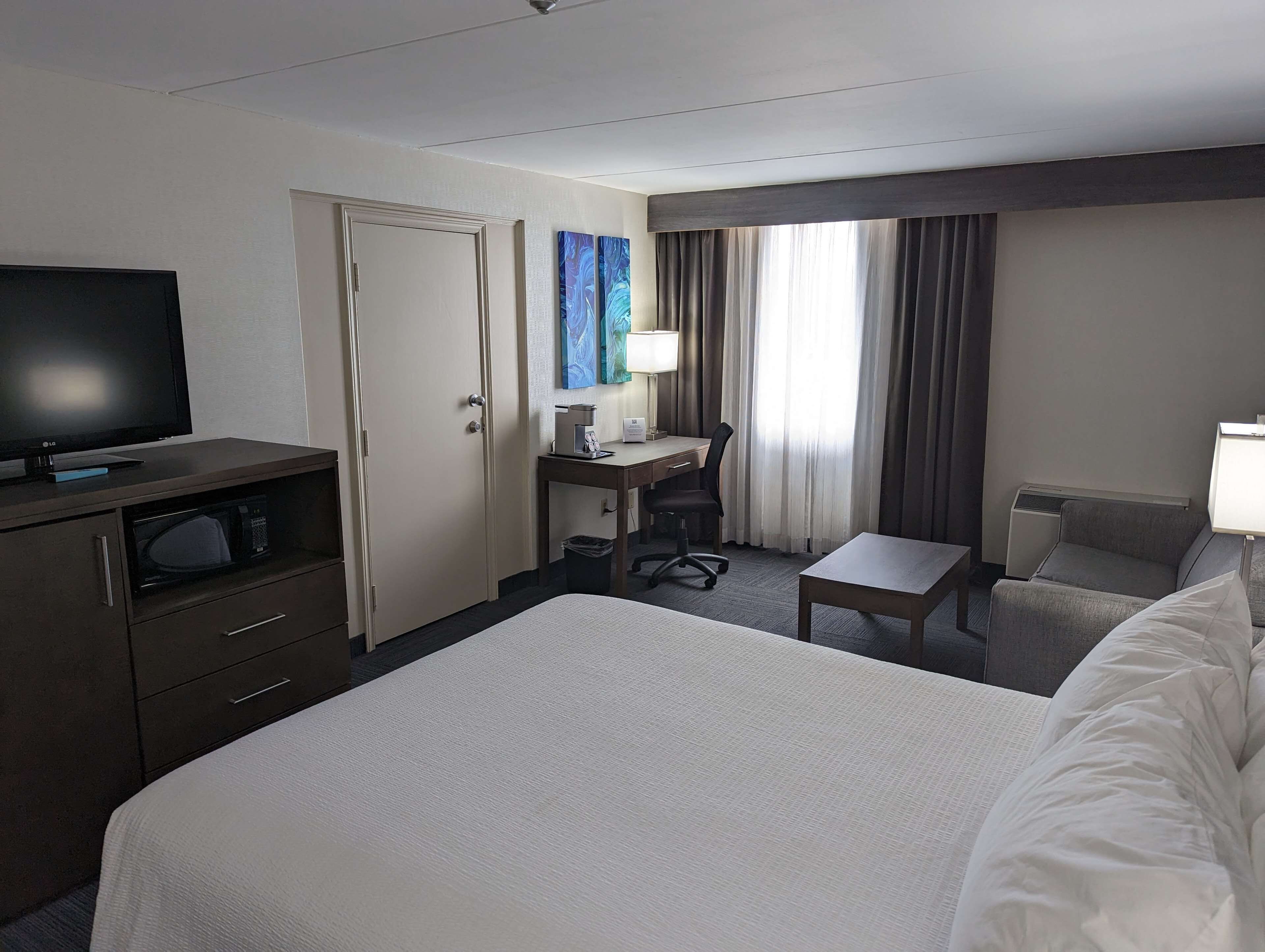 A hotel room with a bed, a desk with a chair, a television, and a window with curtains.