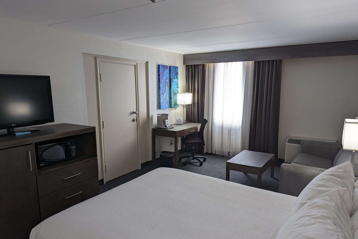 A hotel room with a bed, a desk with a chair, a television, and a window with curtains.