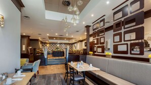 A restaurant with a modern interior, featuring a mix of seating options including tables and booths, and a decorative wall with geometric patterns. - Best Western Plus Toronto Airport Hotel (Mississauga)