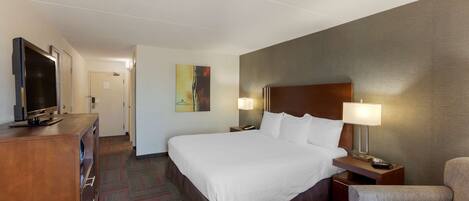 A hotel room with a large bed, a TV, a desk with a lamp, and a red chair.
