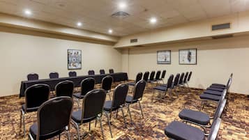 A conference room with a long table and rows of chairs, carpeted floor, and ceiling lights.