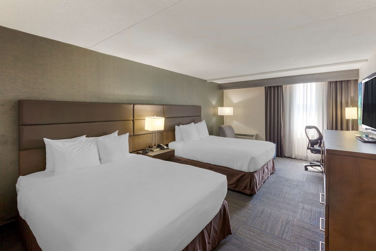 A hotel room with two beds, a desk, a chair, and a television.