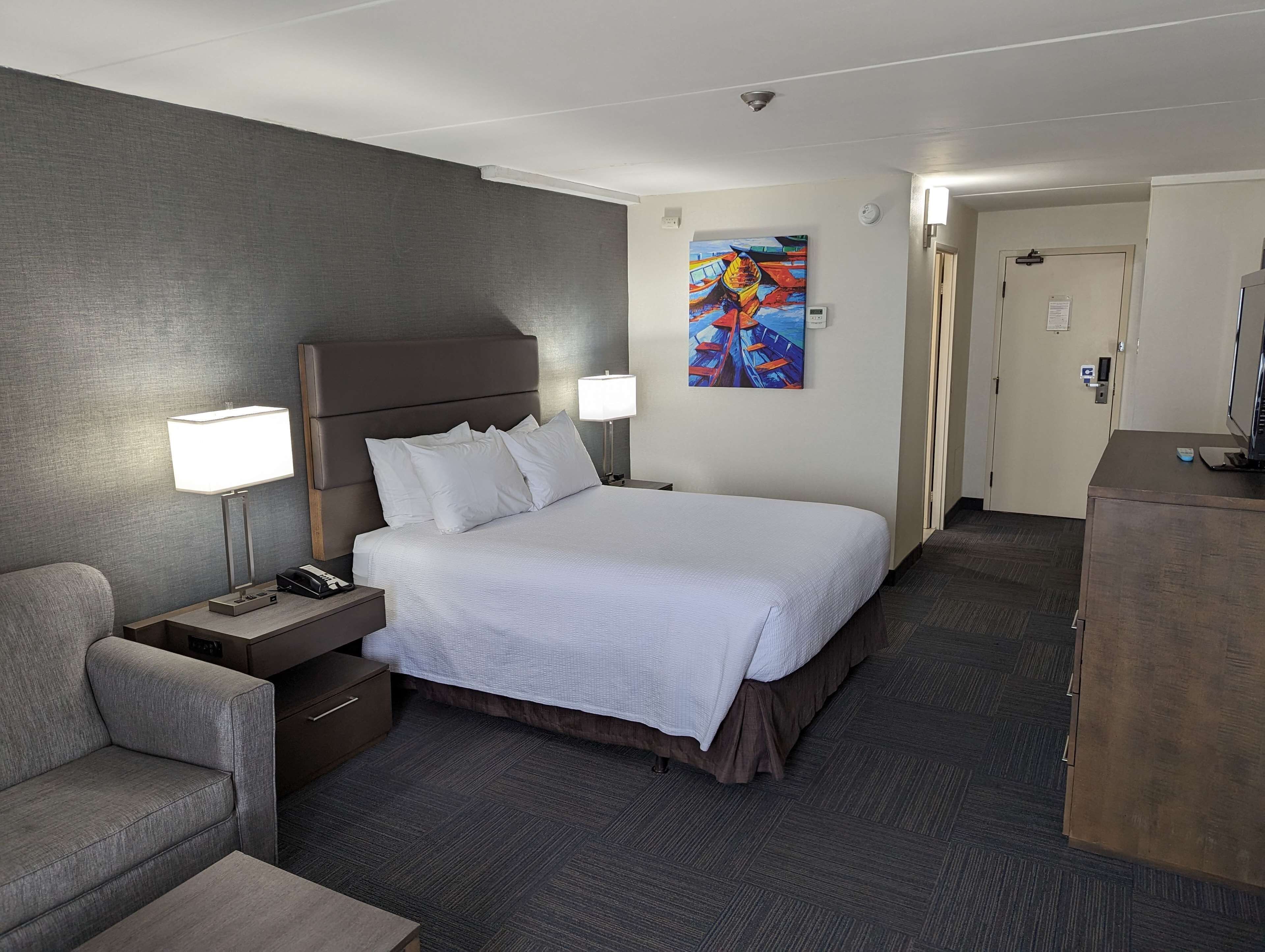 Une chambre d’hôtel avec un grand lit, des lampes de chevet, un bureau avec un téléphone, une chaise et un tableau au mur.