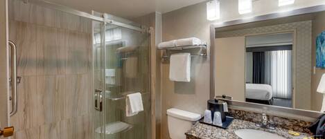 A modern bathroom with a glass-enclosed shower, a toilet, and a sink with a granite countertop.