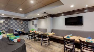 A modern dining area with multiple tables and chairs, a large flat-screen TV mounted on the wall, and a patterned wall design.