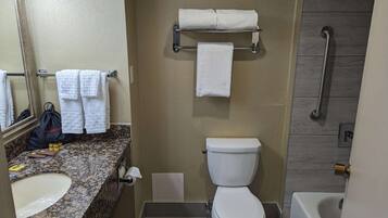 Une salle de bain dotée d’un comptoir en granit, d’un lavabo blanc, de toilettes et d’un espace douche.