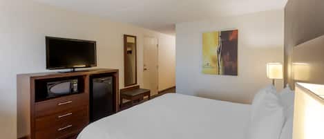 A hotel room with a bed, a TV, a microwave, a desk, and a painting on the wall.