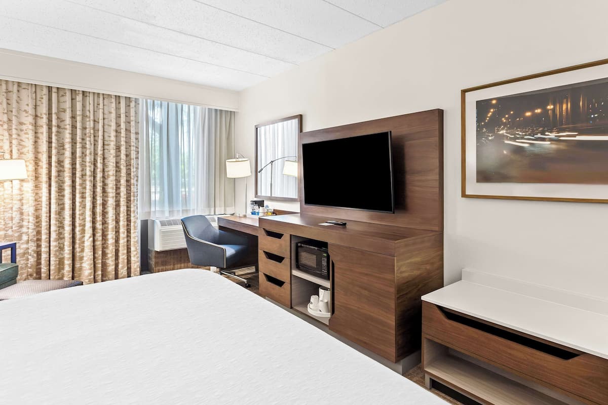 Quarto de hotel com uma cama grande, uma escrivaninha com cadeira, TV de tela plana, micro-ondas e um quadro na parede.