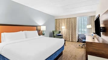 A hotel room with a large bed, a desk, a chair, a lamp, and a TV.