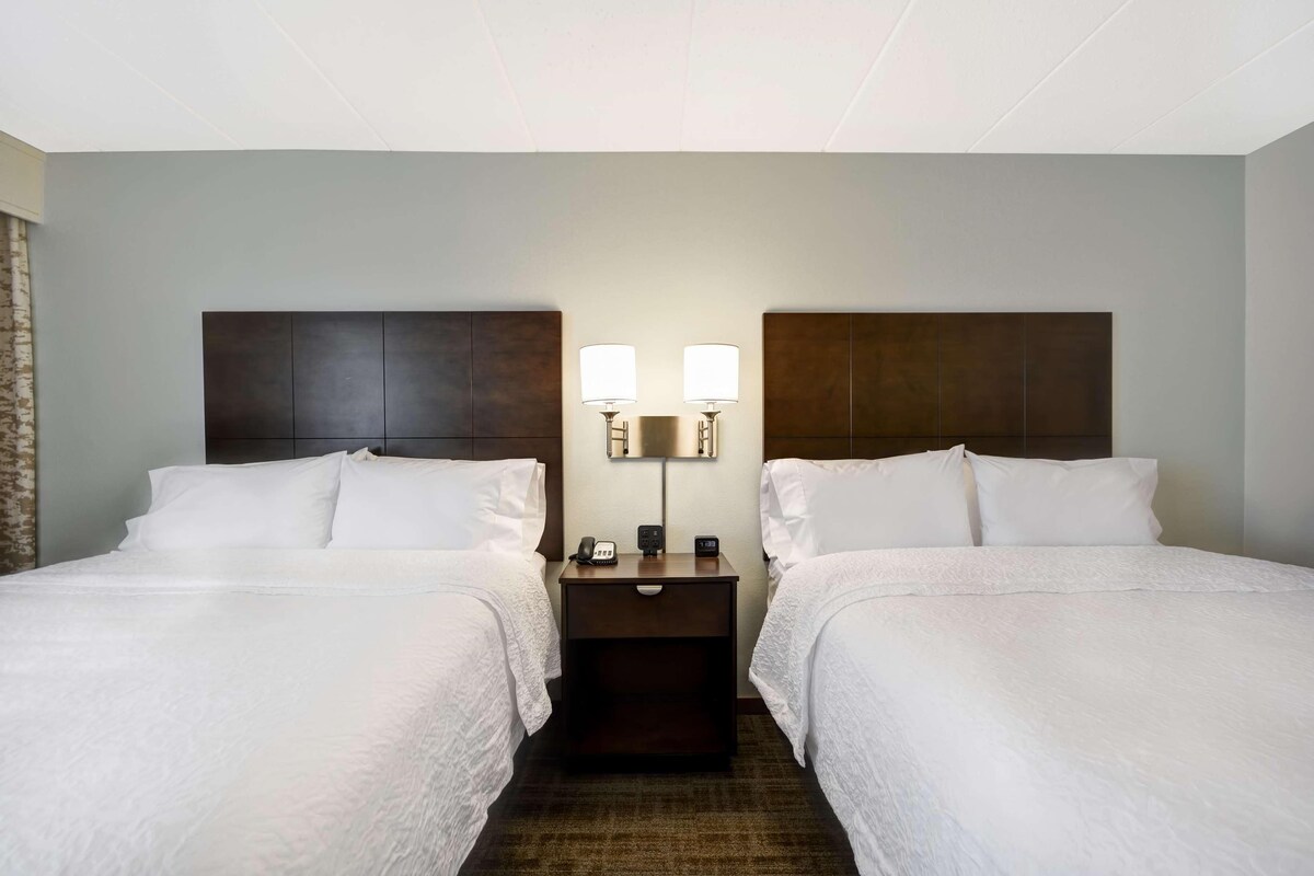 Een hotelkamer met twee bedden, een nachtkastje met een lamp en een aan de muur bevestigd telefoontoestel.