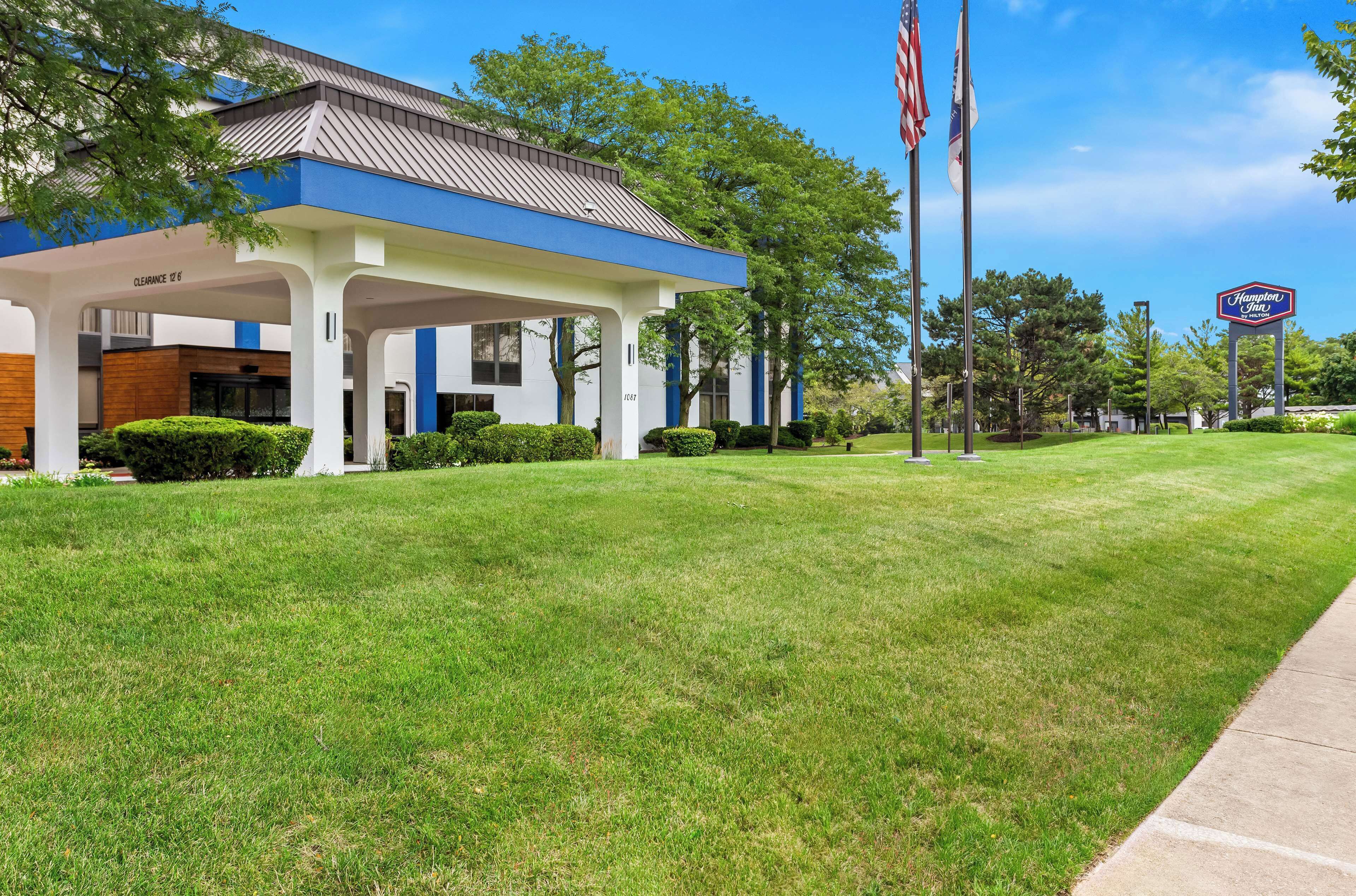 A hotel with a covered outdoor area, a lawn, and a sign for the Hampton Inn.
