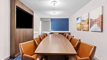 Une salle de conférence avec une longue table en bois, des fauteuils en cuir, un téléviseur à écran plat et des tableaux encadrés accrochés au mur.
