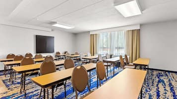 A conference room with multiple tables and chairs, a large screen, and a patterned carpet.