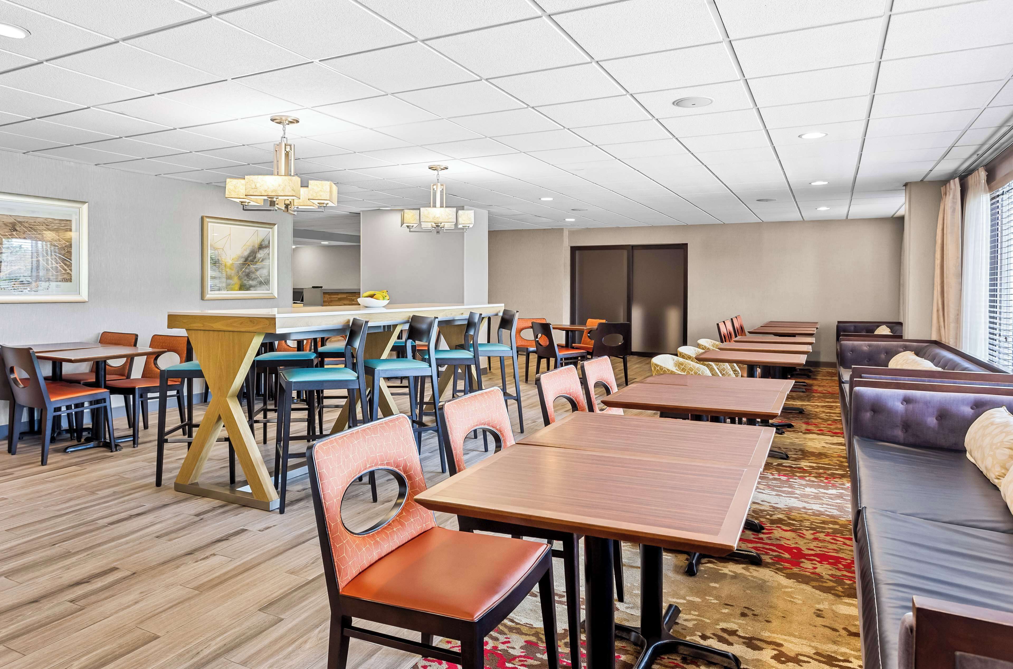 A hotel dining area with multiple tables and chairs, a bar, and a seating area with couches.