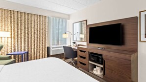 Camera d'hotel con un letto grande, una scrivania con un computer, una TV a schermo piatto, uno specchio e una finestra con tende.