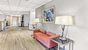 Una hall d'albergo con pavimento in legno, un divano rosa, due lampade, un quadro astratto incorniciato e una reception sullo sfondo.