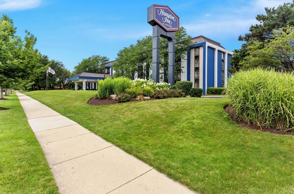 A Hampton Inn by Hilton with a well-maintained lawn, a clear pathway, and a large signboard.
