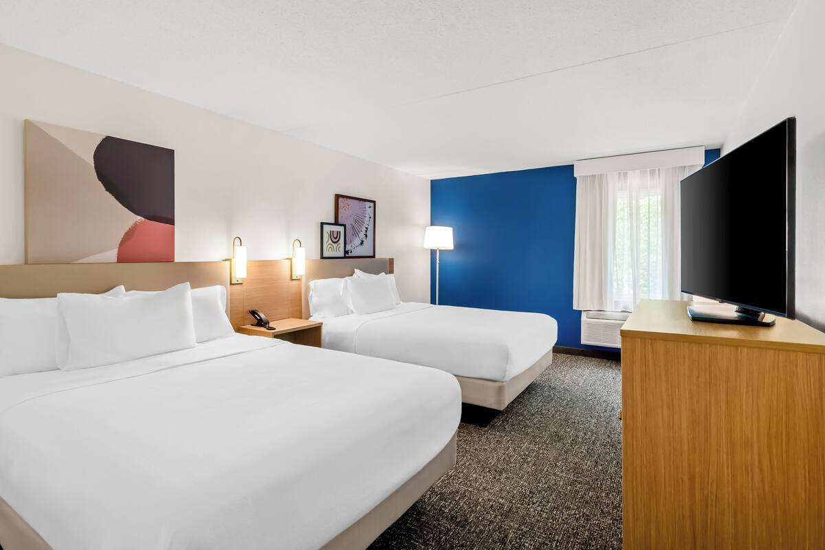 A hotel room with two beds, a TV, a desk, and a window with curtains.