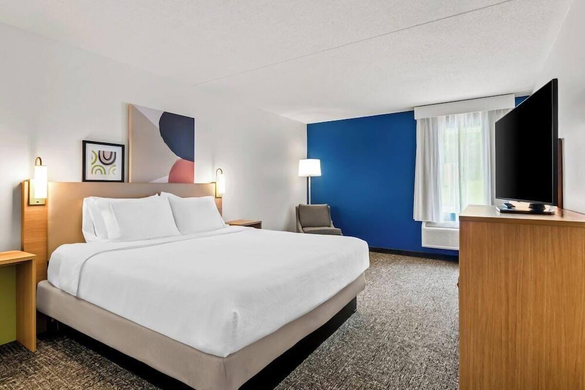 A hotel room with a bed, a desk, a chair, a TV, and a window with curtains.