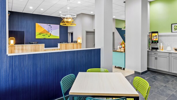 Un intérieur moderne comprenant un comptoir d’accueil, un coin repas avec une table et des chaises, et un espace cuisine équipé d’une machine à café.