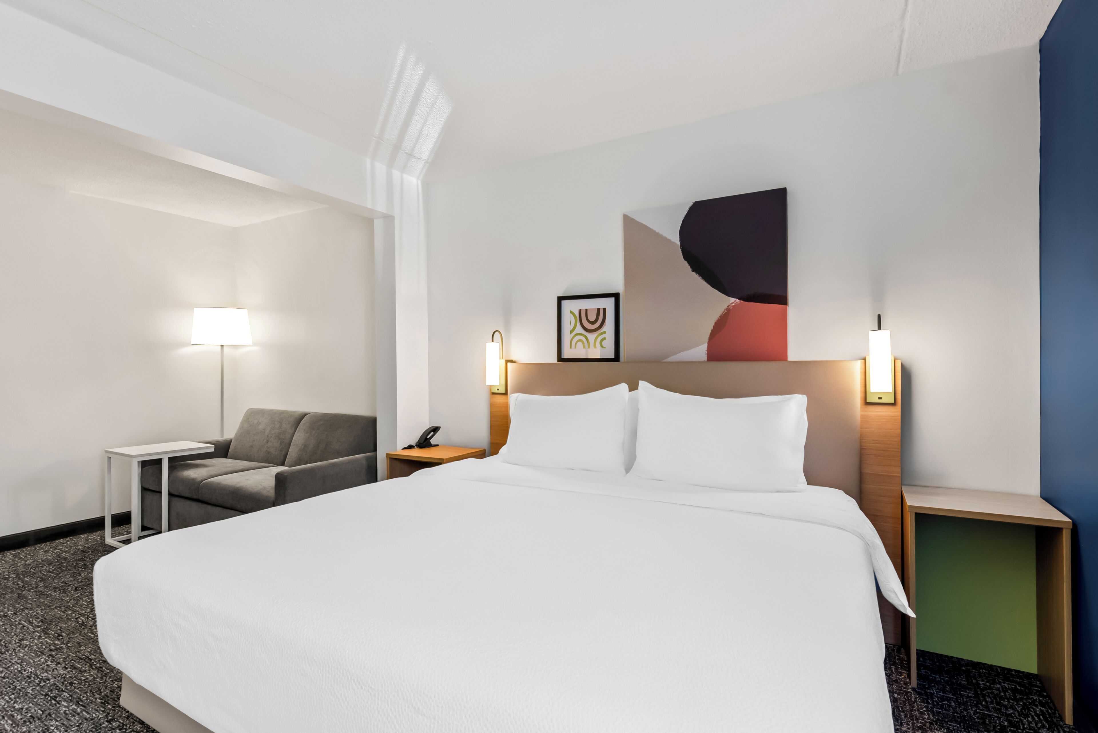 Una habitación de hotel con una cama grande, un escritorio, una silla y una mesita de noche con una lámpara.