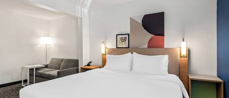 Una habitación de hotel con una cama grande, un escritorio, una silla y una mesita de noche con una lámpara.