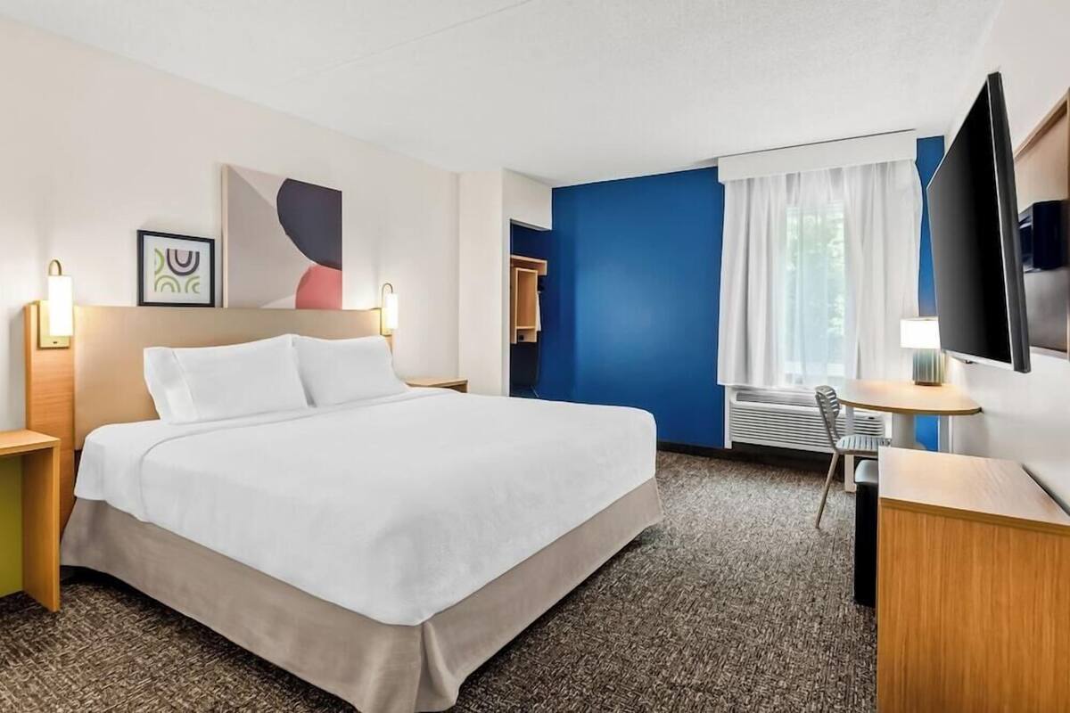 A hotel room with a bed, bedside tables, a desk, a chair, a TV, and a window with curtains.