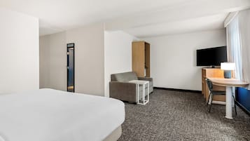 A hotel room with a bed, a desk with a chair, a sofa, a TV, and a window with curtains.
