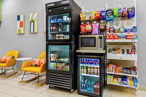 Zona de máquinas expendedoras con opciones de bocadillos, un microondas y asientos con sillas amarillas.