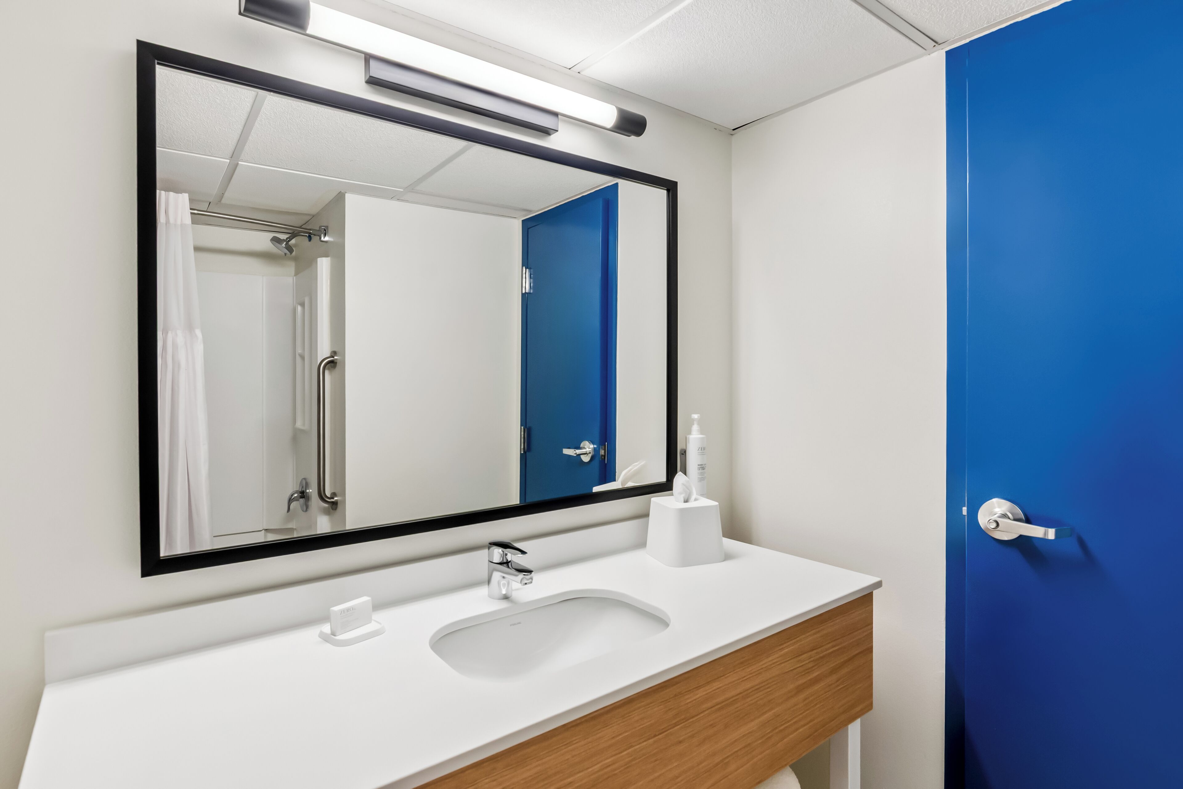 A bathroom with a white sink, a mirror, a blue door, and a shower area.