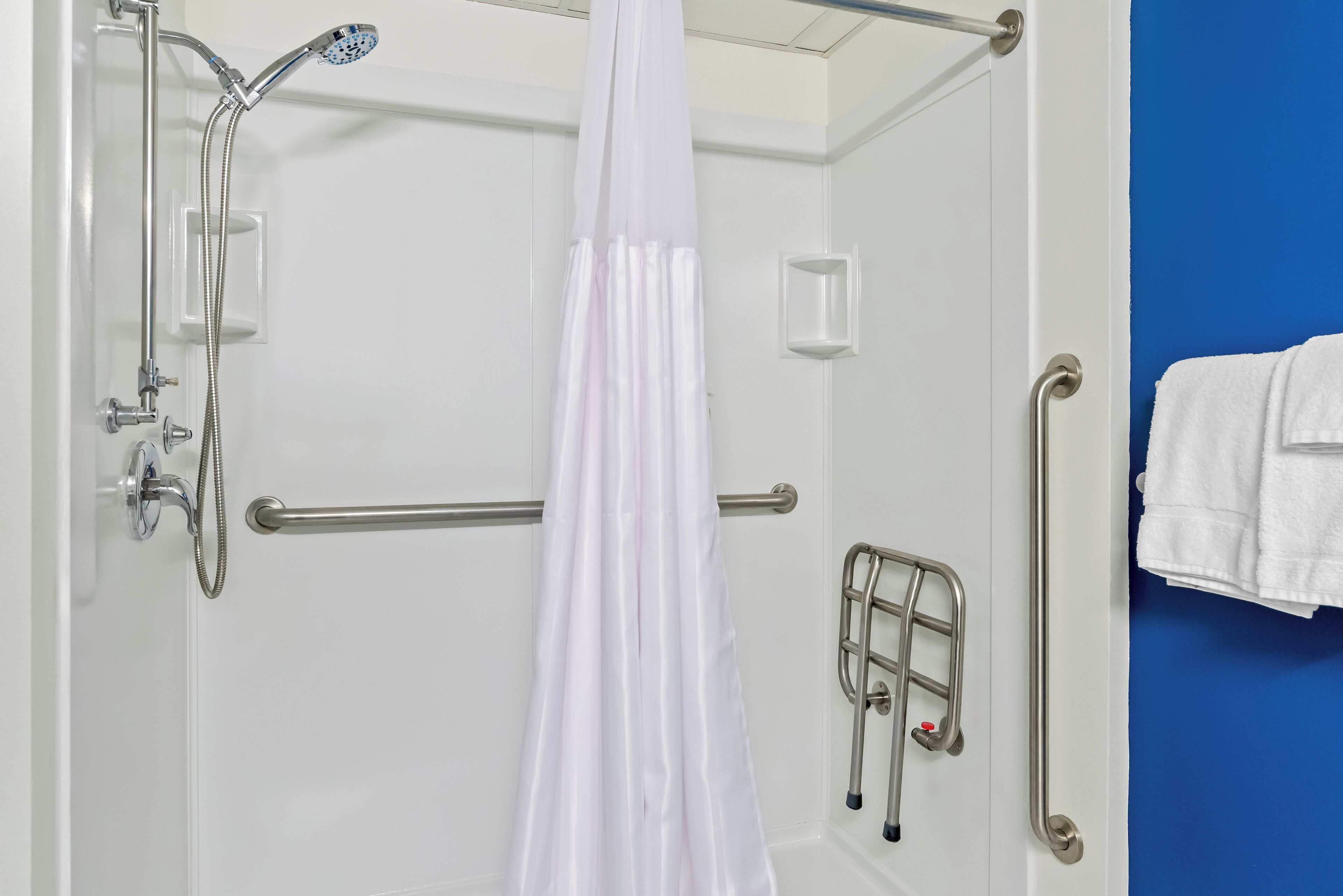 A shower with a handheld showerhead, a glass door, and a white curtain.