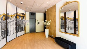 A hallway with a wooden floor, a black bench, a large mirror, and a white vase with flowers.