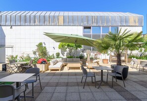 Une terrasse extérieure avec des sièges, une table et un grand parasol.