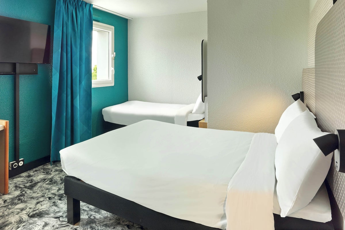 A hotel room with a bed, a desk, a TV, and a window with curtains.