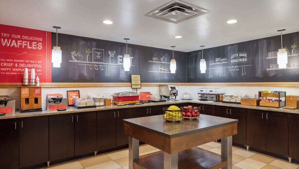 A kitchen area with waffle stations, a table with fruit, and various kitchen appliances. - Hampton Inn Columbus/Dublin (Dublin)