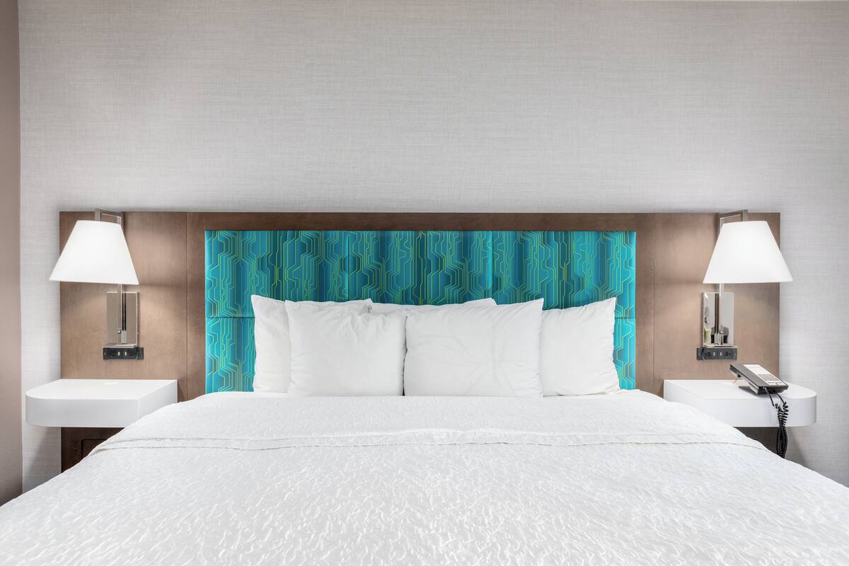 A hotel room with a large bed, two bedside tables with lamps, a wall-mounted phone, and a patterned headboard.