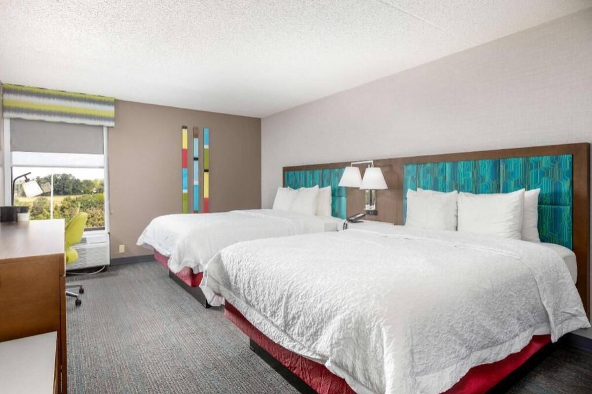 A hotel room with two beds, a desk, a chair, and a window with a view.