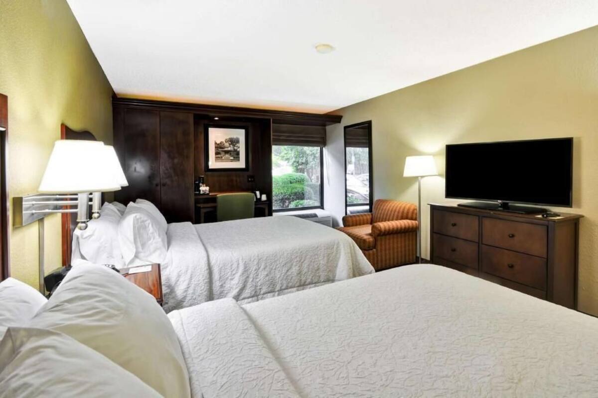 A hotel room with two beds, a television, a desk, and a chair.