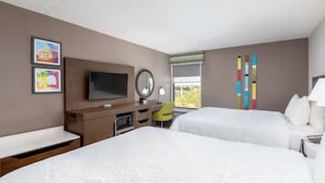 Una camera d'albergo con due letti, una TV, una scrivania con una sedia, una finestra vista e tende verticali colorate.