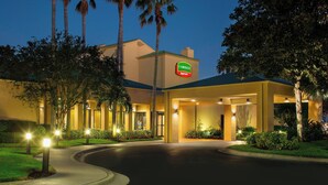 A Courtyard by Marriott hotel entrance at dusk with a well-lit driveway and surrounding greenery. - Courtyard by Marriott Orlando International Dr / Conv Cntr (Orlando)