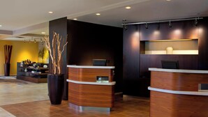 A reception area with two wooden reception desks, a large vase with branches, and a wall-mounted shelf with decorative items. - Courtyard by Marriott Orlando International Dr / Conv Cntr (Orlando)