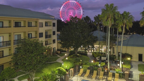A hotel courtyard with a swimming pool, lounge chairs, palm trees, and a Ferris wheel in the background. - Courtyard by Marriott Orlando International Dr / Conv Cntr (Orlando)
