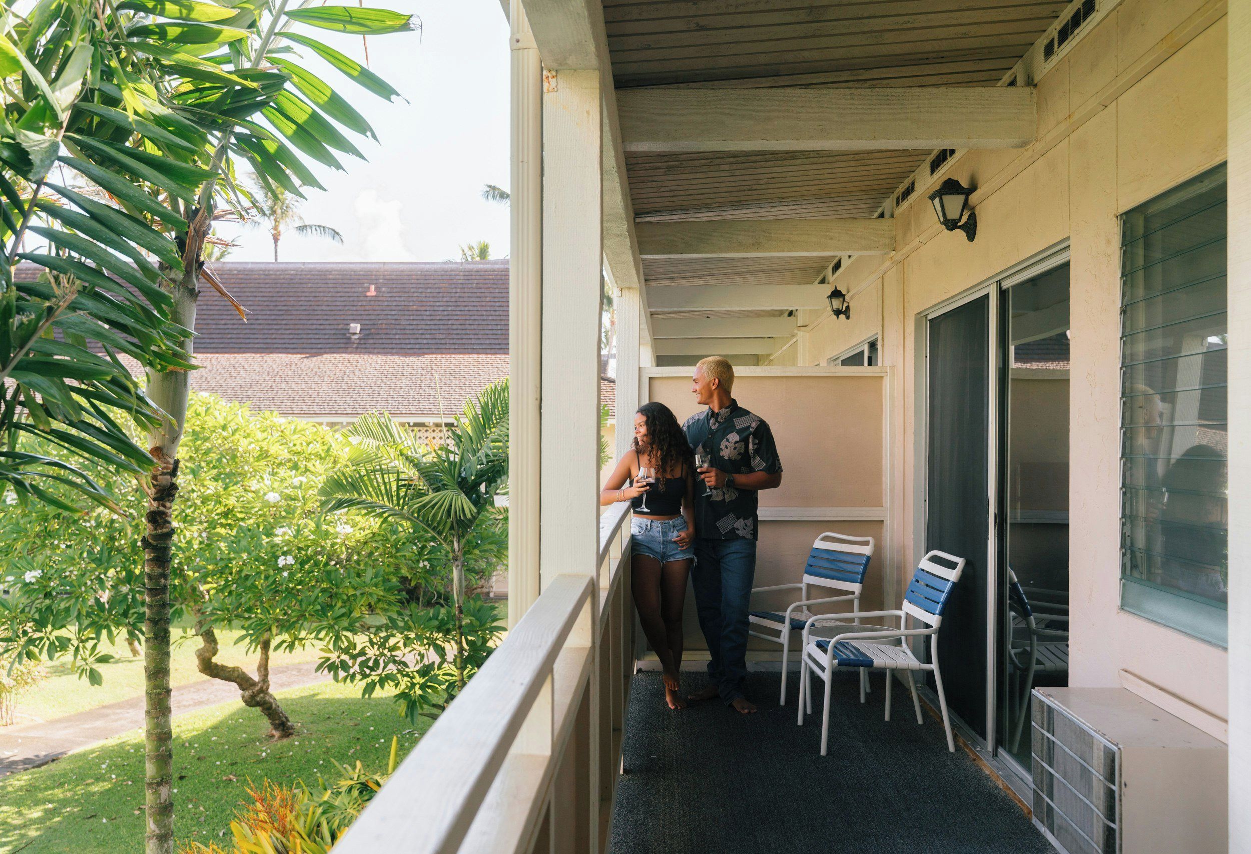 A balcony with a view of a residential area, a railing, and a few chairs.