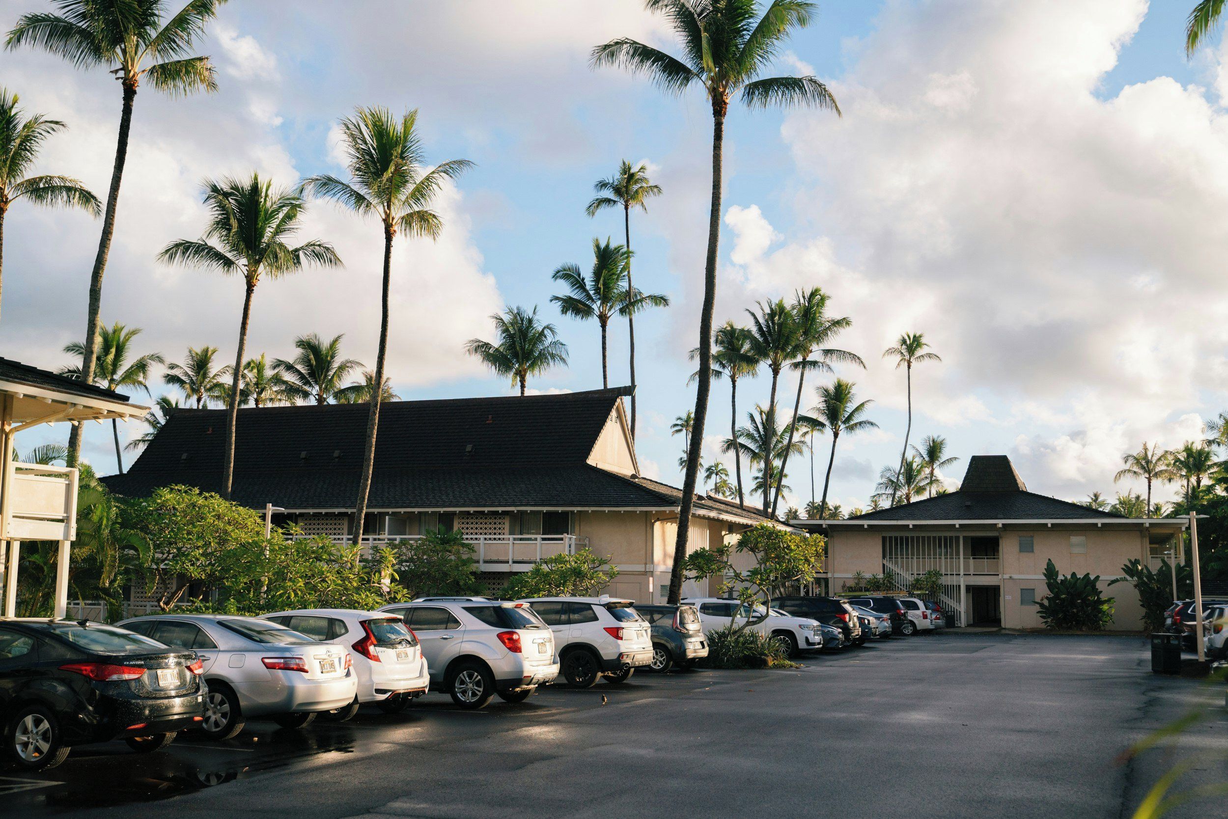 A parking lot with several cars parked in front of a building with a dark roof and white walls.