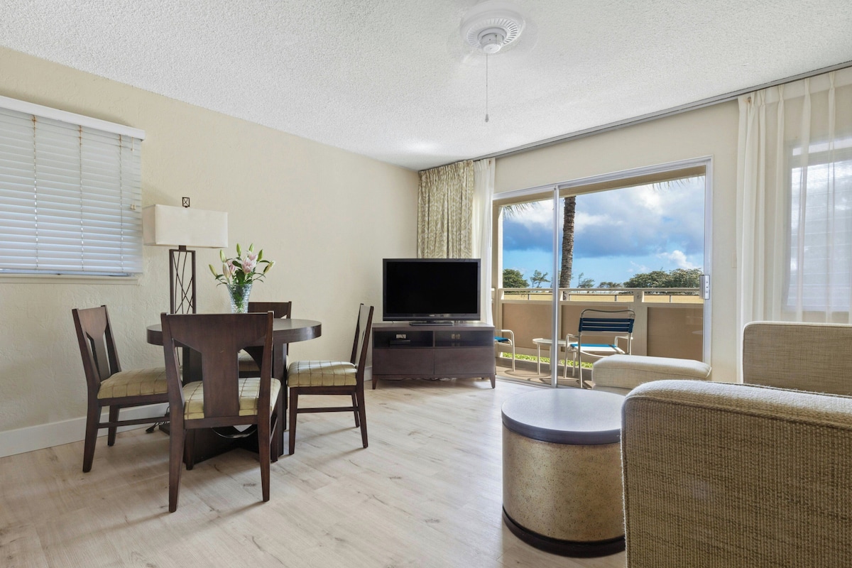 Habitación de hotel con una mesa de comedor, sillas, televisión, sofá y balcón con vistas.