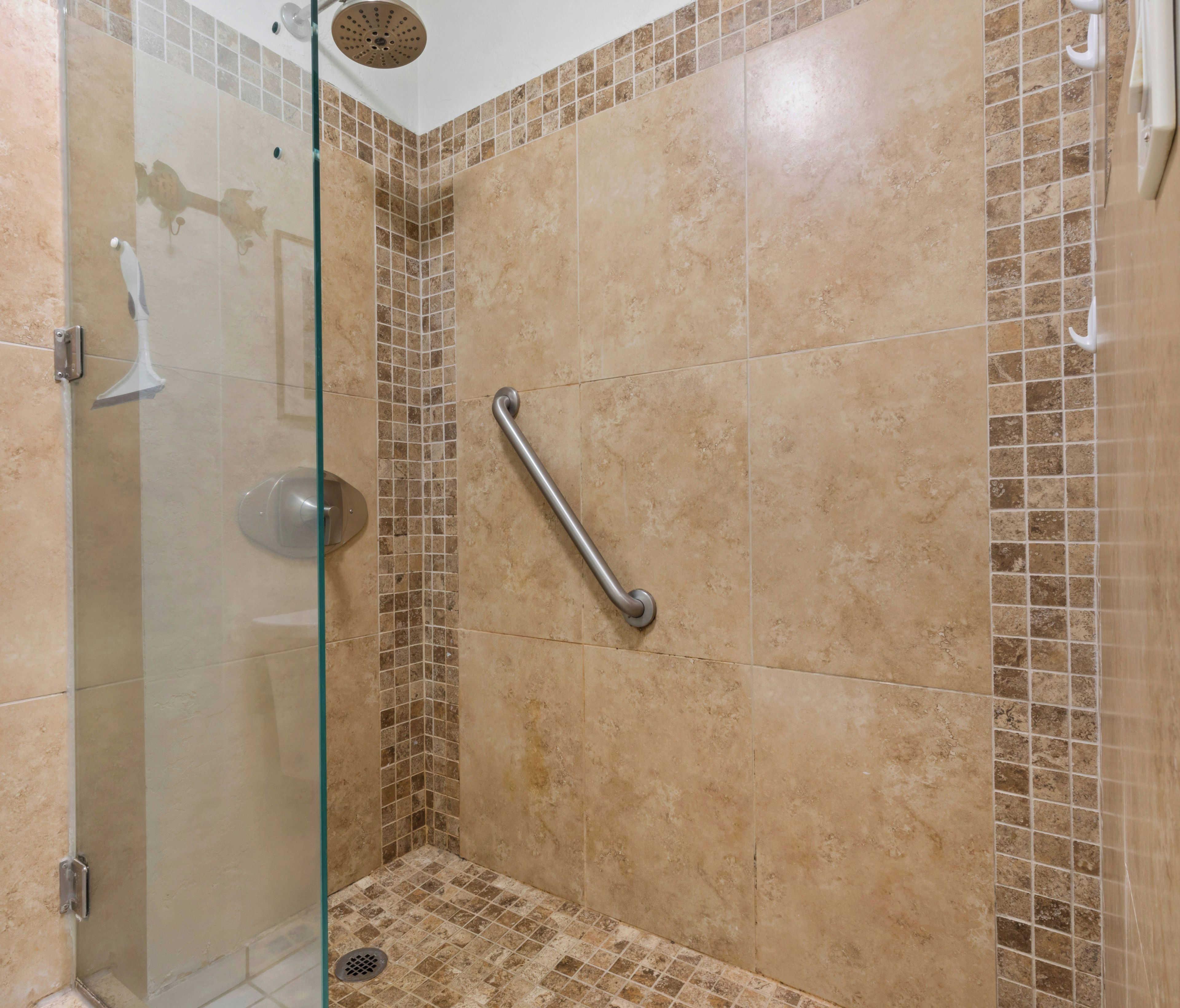 A shower area with a glass door, a handheld showerhead, and a grab bar.