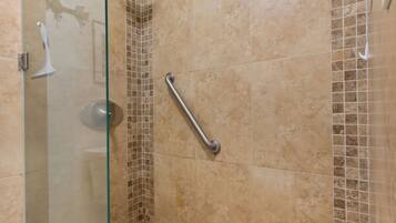 A shower area with a glass door, a handheld showerhead, and a grab bar.