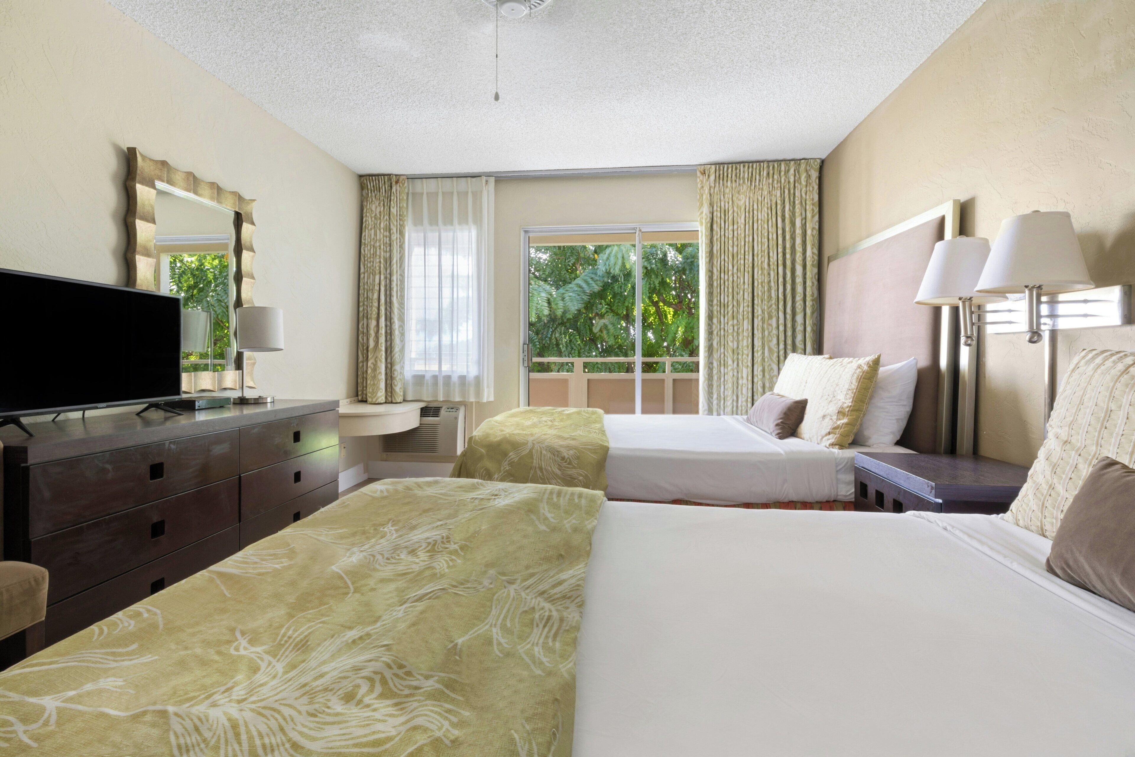 A hotel room with a bed, a television, a dresser, and a window with curtains.