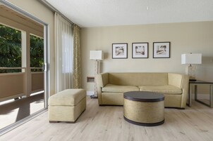 Una sala de estar moderna con un sofá, un reposapiés, una mesa de centro redonda y dos lámparas de pie. Hay tres cuadros en la pared.