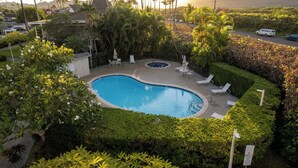 A swimming pool surrounded by lush greenery and palm trees, with lounge chairs and a view of a mountainous landscape. - Plantation Hale Suites (Kapaa)